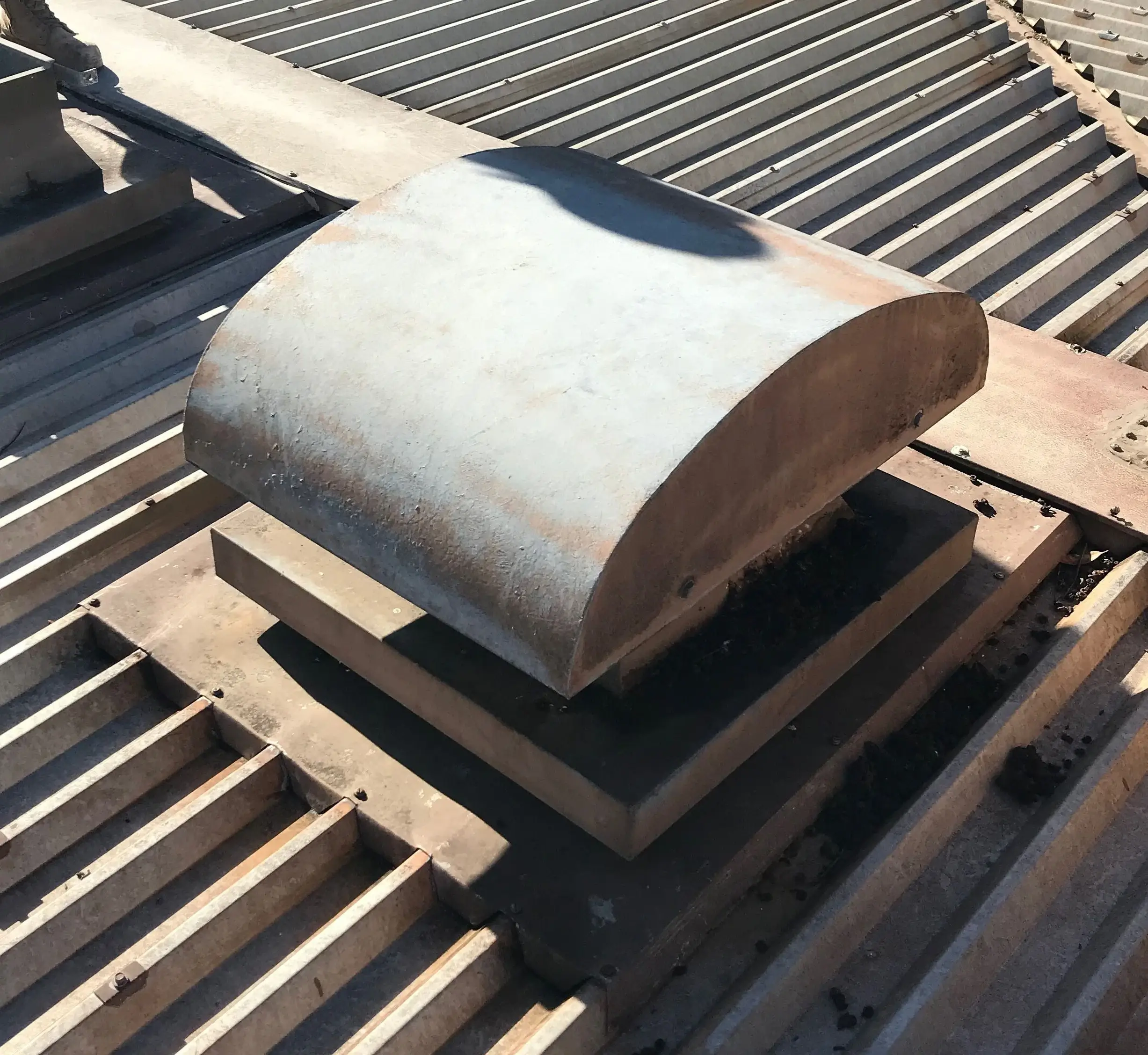 A rusted metal ventilation hood on a corrugated metal roof.